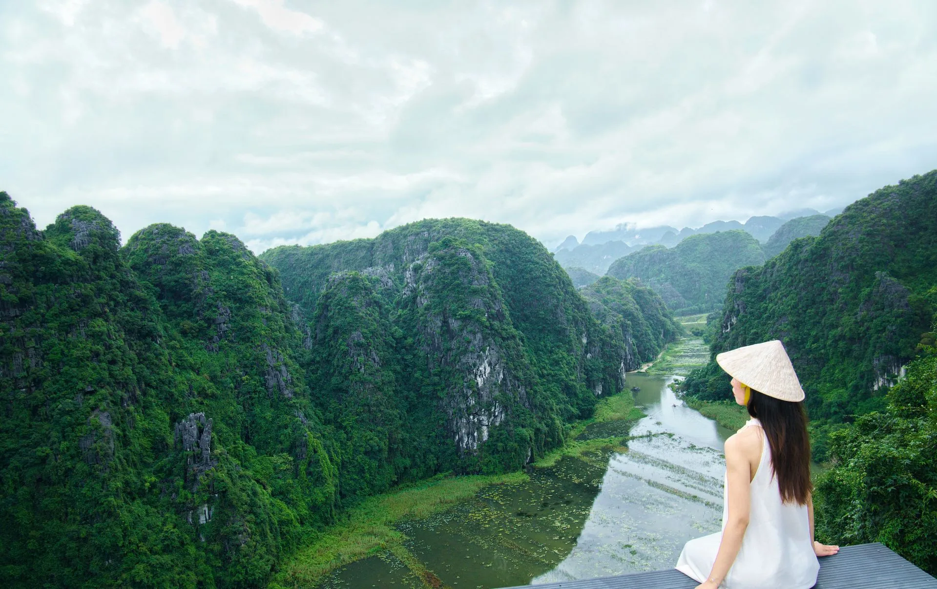 A traveller in a conical hat looking out over the karst valley and river from the Mua Cave viewpoint, Ninh Binh, Vietnam