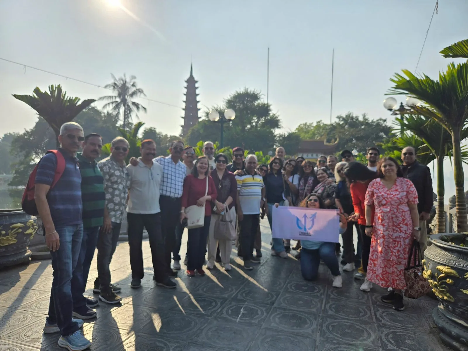 A licensed local guide holding the group flag beside the group at Tran Quoc Pagoda, Hanoi