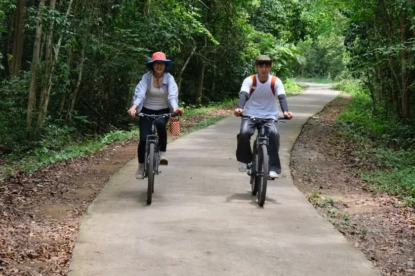 Cyclists on a shaded concrete back lane through the orchards of Ben Tre, Mekong Delta